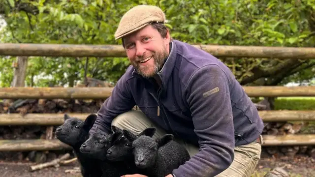 Farmer Tom Martin crouching down with lambs at his farm near Peterborough