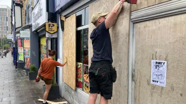 A man takes down the boarding on a shop in Bristol with a tool