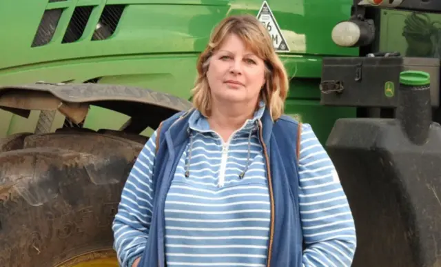 Freya Morgan standing in front of farm machinery wearing a blue and white striped top