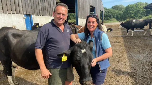 Kaz and Tom Halton stand with one of their cows in an enclosure.