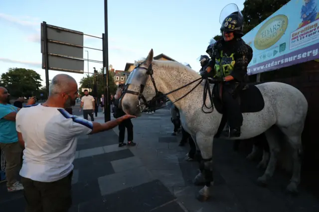 A member of the public feeds a police horse as officers stand on duty near a counter demonstration against an anti-immigration protest called by far-right activists, outside the United Immigration Services offices at The Beacon in Newcastle-upon-Tyne, north-east England on August 7, 2024.