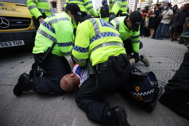 Police officers arrest a man at a riot in Liverpool, as he is pinned on the ground and the three officers restrain and cuff him.