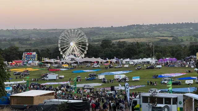 Ashton Court. There is a field full of people, with a ferris wheel, canopies and hot air balloons which are not yet inflated.