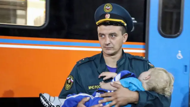 A Russian Ministry of Emergency Situations staff member holds a child