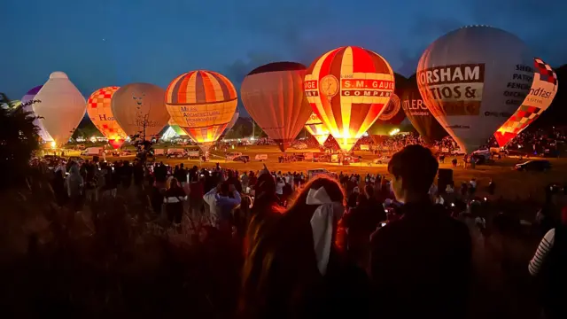 Hot air balloons. They are inflated but tethered to the ground. They are lit up with fire.