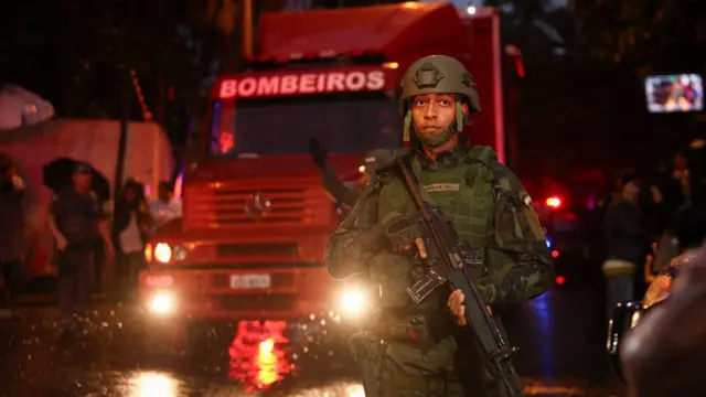 A member of security forces dressed in camouflage and a hard hat stends guard near the site of the plane crash in Brazil