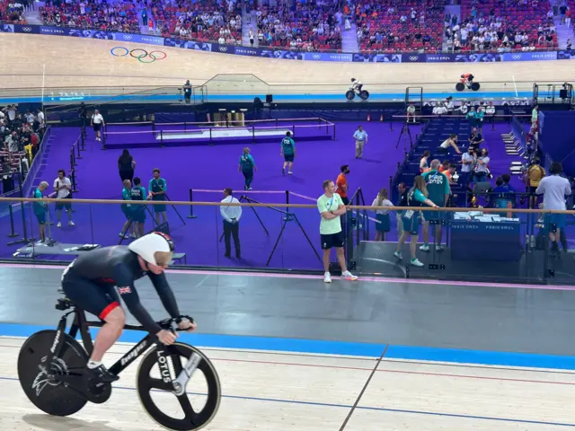 Jack Carlin rides on the track while Sir Jason Kenny watches on