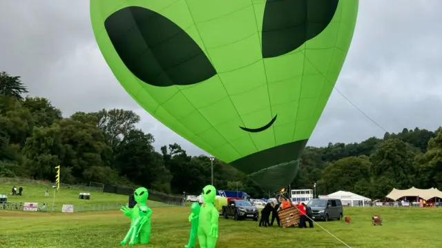 Alien balloon and people in alien costumes stood in a field