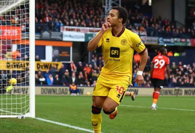 Cameron Archer, wearing Sheffield United's away yellow kit, puts his finger to his lips in celebration after scoring against Luton.