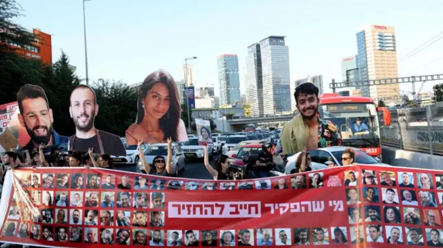 Protesters hold a banner with images of hostages against a cityscape