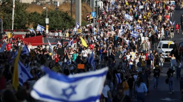 Large group of protestors in Jerusalem, with an Israel flag in the foreground