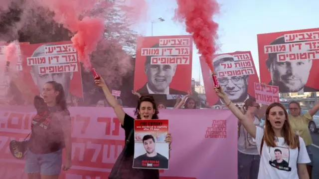 Protesters hold posters while holding flares emitting pink smoke