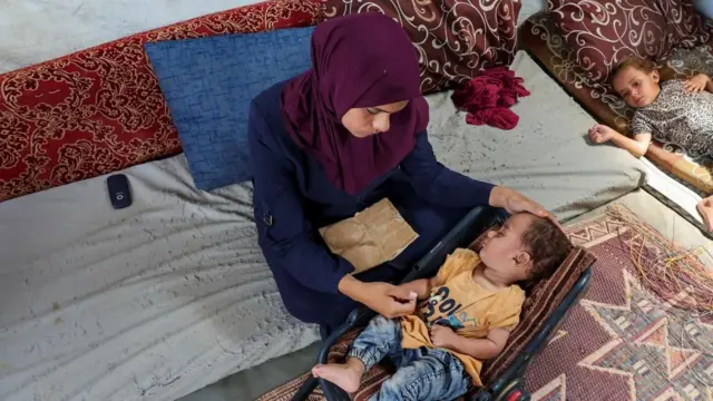 A woman looks over a child sleeping in a car seat. The child is wearing jeans and a yellow top