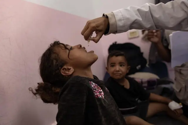 Health worker gives a young child oral drops as she opens her mouth with her head titled back