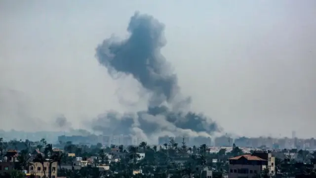 Wide shot of a town with plumes of smoke rising to the sky