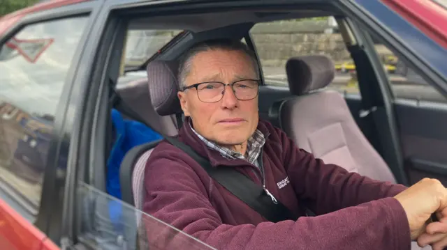 A 70-year-old man Andrew waiting in a red car