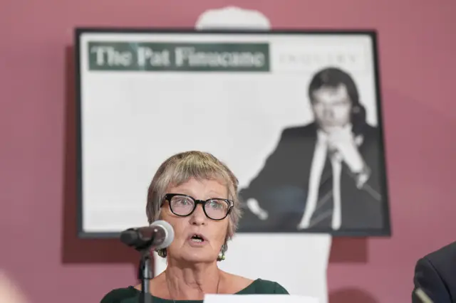 Geraldine wearing a green dress and wearing black glasses address press.