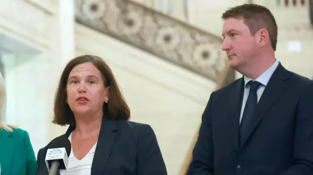 Mary Lou McDonald and John Finucane standing in front of a microphone