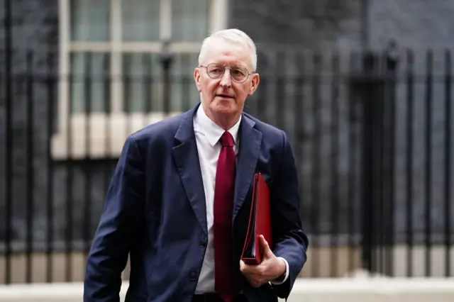 Man with grey hair and glasses walking on the street with a blue jacket with a red tie and white shirt.