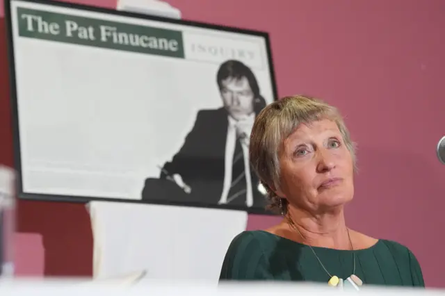 Geraldine in a green dress with picture of her late husband pat behind her in a framed picture