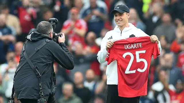 Manuel Ugarte poses with a Manchester United shirt on the Old Trafford pitch