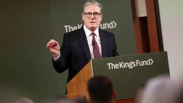 Starmer genstures with his right hand as he speaks at a lectern