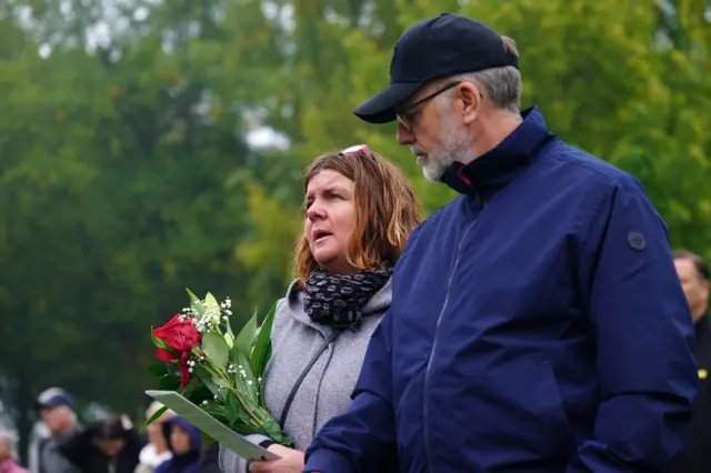 Many of those gathered outside have brought flowers and are holding orders of service