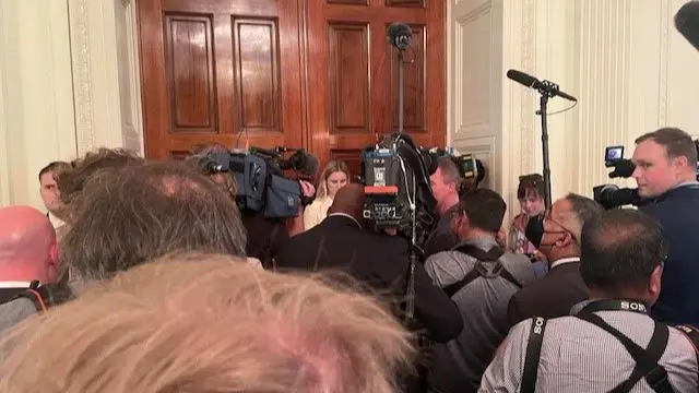 A crowd of reporters are seen waiting outside a door at the White House