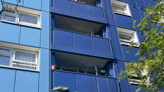 A woman is just visible on her blue coloured balcony. Windows are on either side. The balconies are covered in a safety netting.