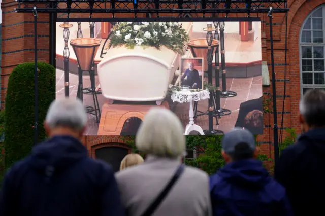 The funeral service is being displayed on a large screen outside the church