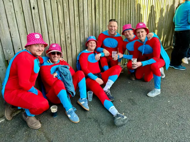 A group of men in fancy dress sitting by a fence