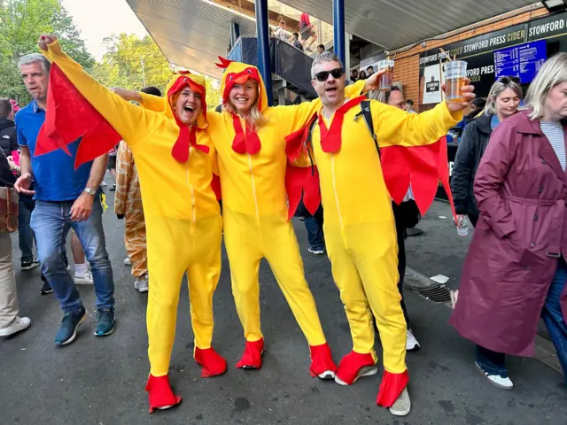 Two women and a man, all dressed in chicken outfits