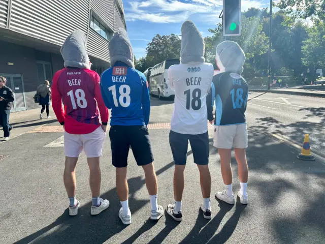 Sussex fans wearing shark heads and with their backs turned to show Beer 18 on the backs of their shirts