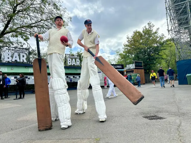 Two performers on stilts dressed as cricketers