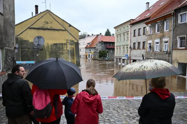 People carrying umbrellas look at flooded streets after heavy rainfall in Bystrzyca Klodzka, southwestern Poland