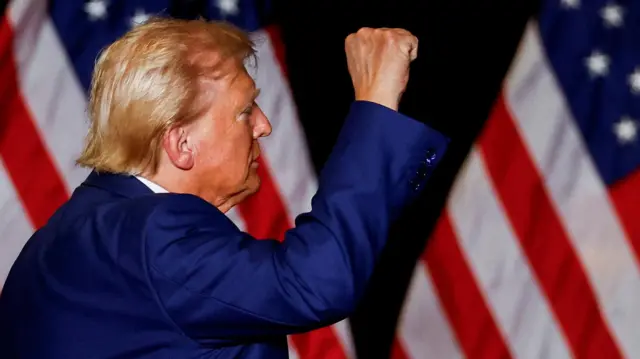 Trump holds up a single first in front of two US flags