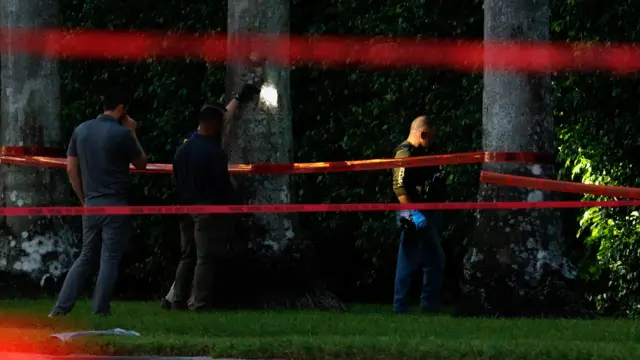 Law enforcement officers work near the shrubbery on the perimeter of Trump's golf course