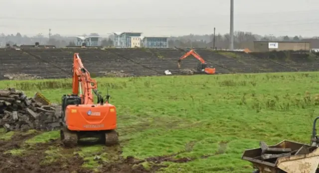 Orange digger digging up Casement Park