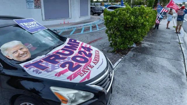 A parked car with the slogan "TRUMP 2024: Save America" on its bonnet, alongside a cutout of Trump's face