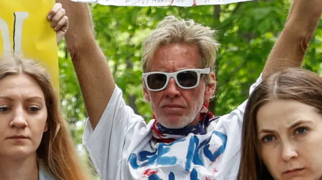 Ryan Wesley Routh standing with his hands raised as he attends pro-Ukraine rally wearing white sunglasses