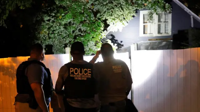 Secret Service and Homeland Security agents check a home with torch shining in darkness onto fence and window