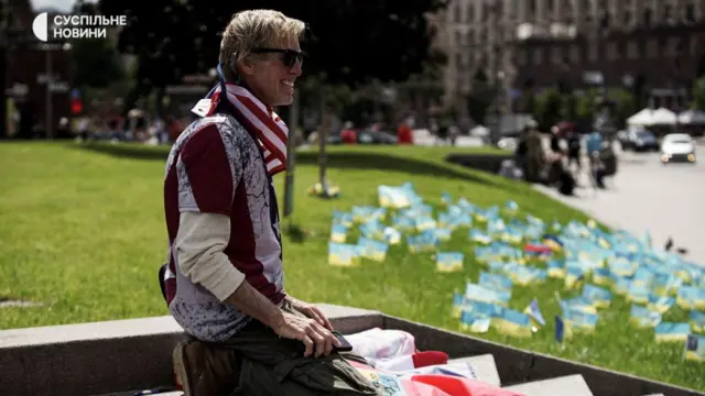 Ryan Wesley Routh knelt down with lots of small Ukraine flags scattered amongst a grass verge