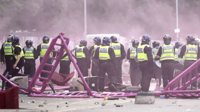 Line of police in front of pushed over barriers