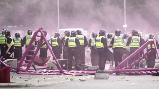 Line of police officers surrounded by stones and rocks and overturned barriers