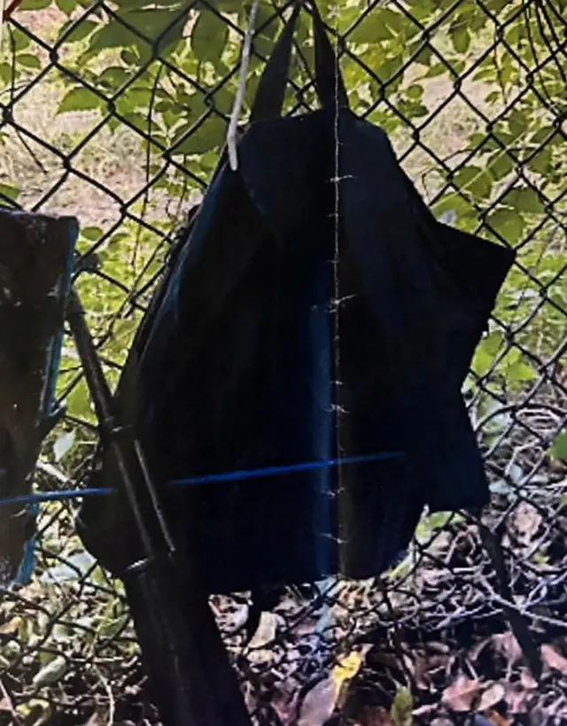 Bags hang from a fence over a rifle propped against it,