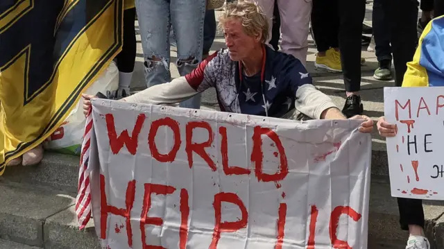 Ryan Wesley Routh holding banner saying 'world help us' written in red on white background