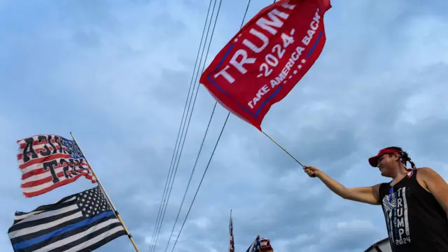 A woman waving a flag that says "Trump 2024: Take America back"