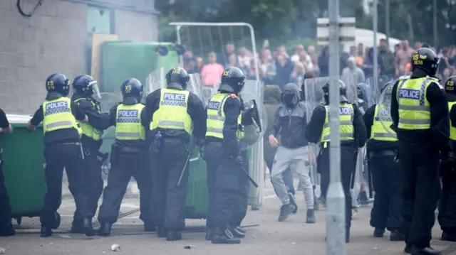 Riot police in a line peer at masked protesters approaching them