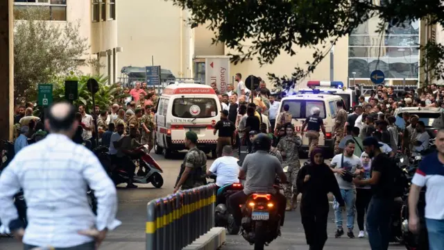 Ambulances pass through a crowd outside a hospital, with armed soldiers present