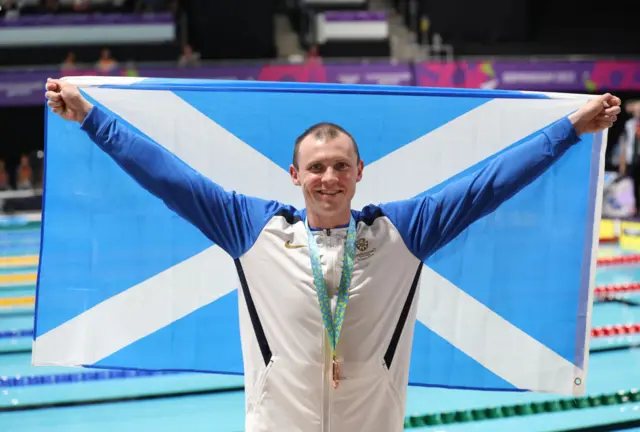 Swimmer Ross Murdoch waves a Scottish flag after winning a Commonwealth Games medal